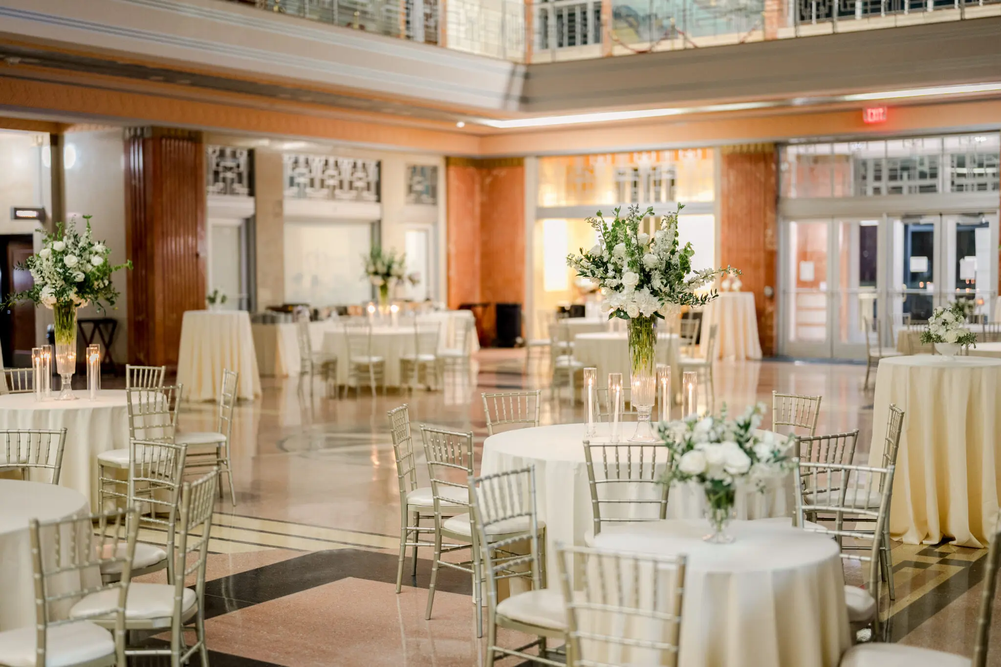 Wedding reception setup with round tables, white floral centerpieces, cocktail tables, and silver Chiavari chairs at Messina’s at the Terminal in New Orleans.